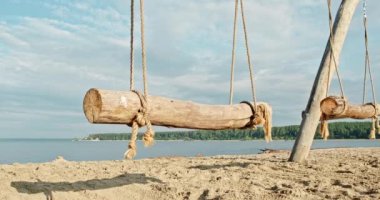 Deniz kıyısında, okyanusta sallan. El yapımı ahşap salıncaklar, şafak vakti baraj gölünün kıyısında insanlar olmadan. Kumlu sahilde el işi sallama. Salıncakta sallanmak