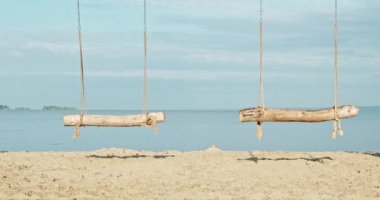 Deniz kıyısında, okyanusta sallan. El yapımı ahşap salıncaklar, şafak vakti baraj gölünün kıyısında insanlar olmadan. Kumlu sahilde el işi sallama. Salıncakta sallanmak