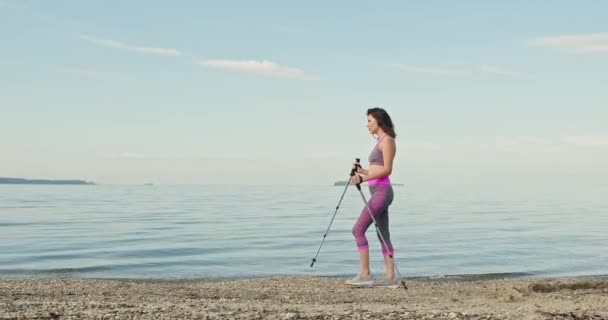 Юная спортсменка занимается спортивной ходьбой на треке. Женщина в спортивном костюме занимается на пляже морем. Девушка тренируется утром на пляже. Концепция спортивной ходьбы — стоковое видео
