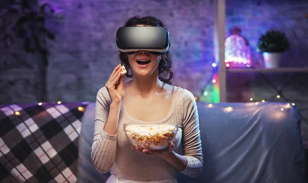 Ragazza ottenere esperienza VR auricolare sta utilizzando occhiali realtà aumentata di essere in realtà virtuale. Giovane donna indossare VR auricolare e guardare film con popcorn a stare a casa — Foto Stock