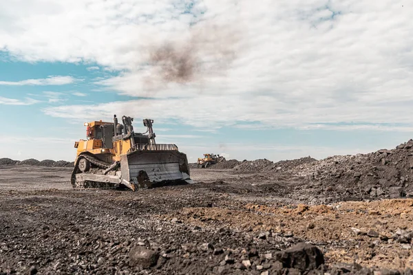 Excavadora amarilla en carrera se mueve sobrecarga. Bulldozer peina el suelo, con el sol brillante y el cielo azul agradable en el fondo —  Fotos de Stock