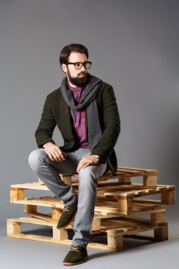 Paletler üzerinde oturan bir ceket giyen genç şık adam sakallı,