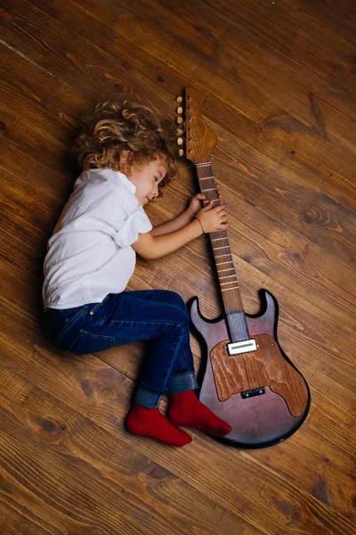 Pequeño niño durmiendo y abrazando guitarra — Foto de Stock