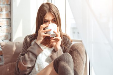 Kupası ile bir pencere üzerinde oturan kadın