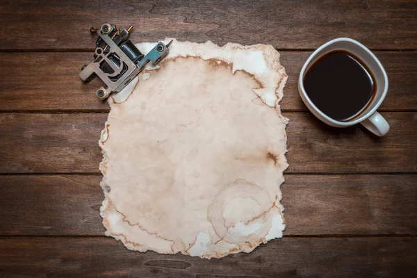 Máquina para tatuagem perto de papel velho e xícara de café — Fotografia de Stock