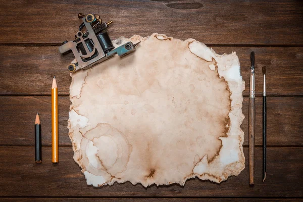 Tätowiermaschine in der Nähe von altem Papier und zwei Pinsel mit zwei Bleistiften — Stockfoto