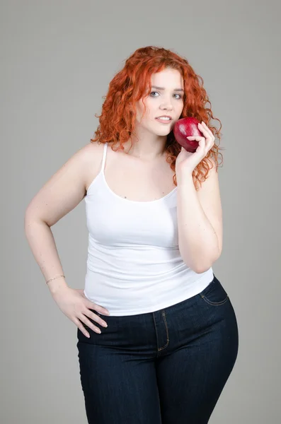 Hermosa chica gorda con el pelo rojo con manzanas en las manos sobre fondo gris — Foto de Stock