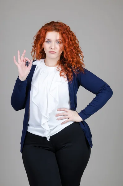 Hermosa chica gorda con el pelo rojo en un traje de negocios sobre un fondo gris — Foto de Stock