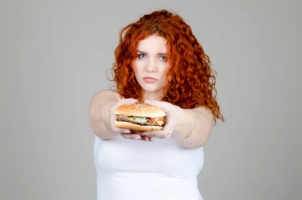 Bella ragazza grassa con i capelli rossi con Burger in mano su sfondo grigio — Foto Stock