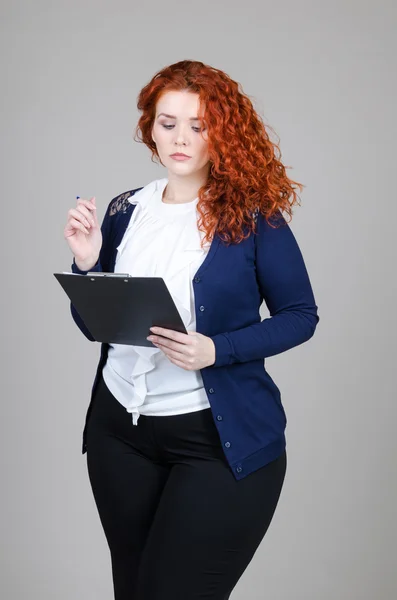 güzel şişko kız Kızıl saçlı tablet ile iş takım elbiseli ve gri arka plan üzerinde onun elinde kalem