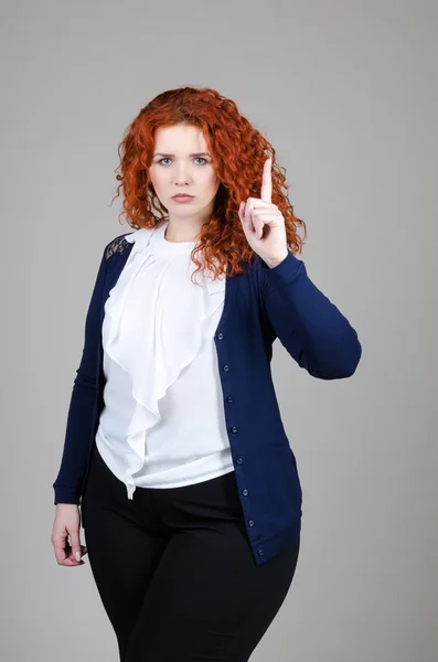 Bella ragazza grassa con i capelli rossi in un abito da lavoro su uno sfondo grigio — Foto Stock