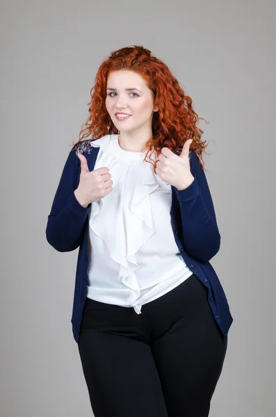 Hermosa chica gorda con el pelo rojo en un traje de negocios sobre un fondo gris — Foto de Stock