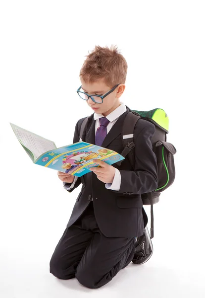 Lindo niño con mochila leyendo un libro en el suelo, aislado sobre fondo blanco — Foto de Stock