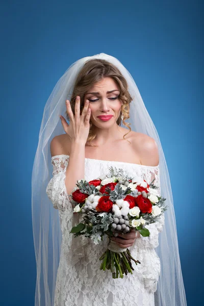 Jovem menina bonita em um vestido de noiva com um véu com um buquê de flores nas mãos sobre fundo azul — Fotografia de Stock