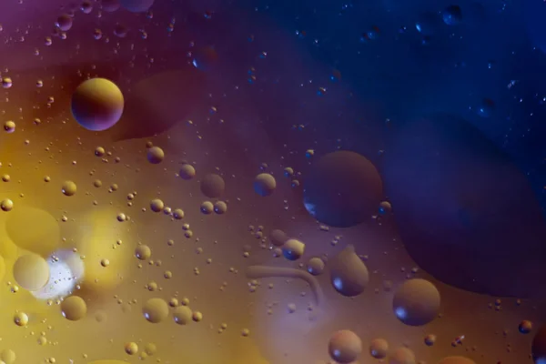Drops of vegetable oil in water on a multi-colored background. The drops resemble planets in outer space.