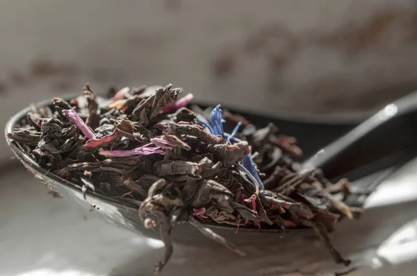 Pembe ve mavi yapraklı siyah çay eski pencere pervazında siyah bir kaşıkta.