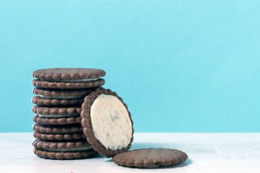 Masada bir yığın çikolatalı kurabiye var. Yanında kırık bir kurabiye var. Arkaplan rengi kahverengi.