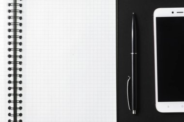 Açık bir defter, siyah bir kalem ve arka planda beyaz bir akıllı telefon..