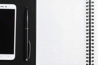 Açık bir defter, siyah bir kalem ve arka planda beyaz bir akıllı telefon..