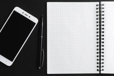 Açık bir defter, siyah bir kalem ve arka planda beyaz bir akıllı telefon..