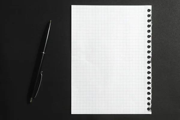 A white piece of paper from a notebook and a black pen on a dark background.