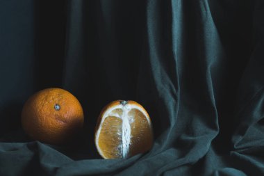 Yeşil bir bezin kıvrımlarında iki olgun portakal. Bir portakal ikiye bölünmüş. Düzgün beslenme ve sağlıklı yaşam tarzı kavramı..