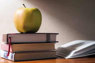 Yeşil elma üç kitabın üzerinde. Onun yanında açık bir kitap var..