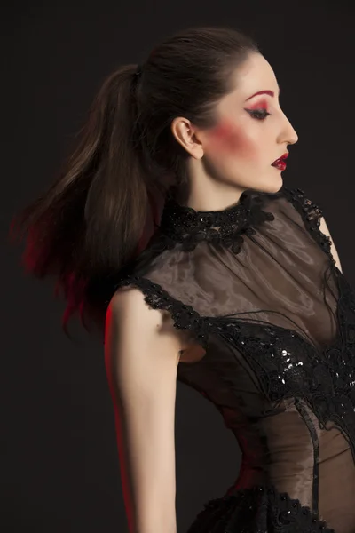 Karanlık bir arka plana dayanır kırmızı ile vurgulanacaktır, siyah elbiseli güzel genç esmer kadın portresi — Stok fotoğraf