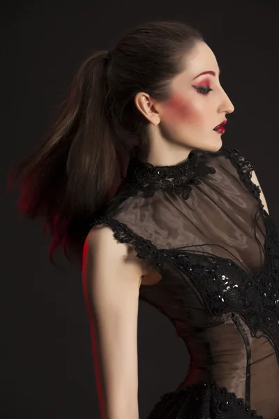 Portrait of beautiful young brunette woman in black dress against dark background, highlighted with red — Stock Photo, Image