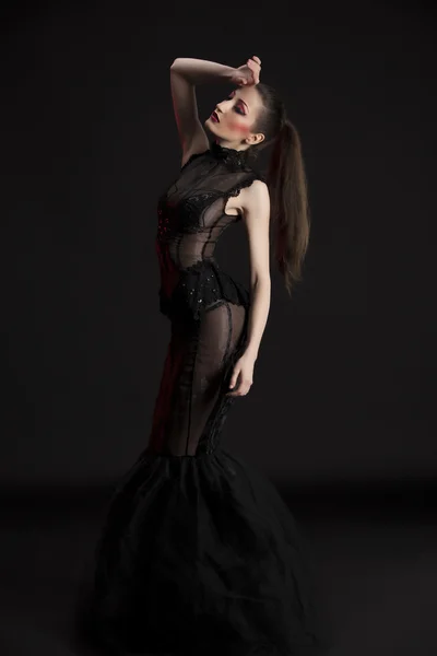美丽年轻的黑发女人，穿着黑色的连衣裙，在黑暗的背景下，用红色突出显示的肖像 — 图库照片