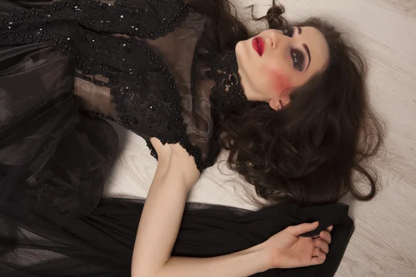 Portrait of beautiful young brunette woman princess in black dress lying down on floor — Stock Photo, Image