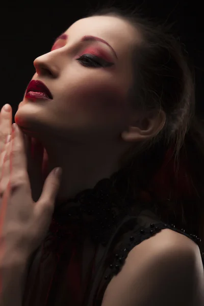 Retrato de una hermosa joven morena en vestido negro sobre fondo oscuro, resaltado con rojo. Retrato de primer plano, ojos cerrados — Foto de Stock
