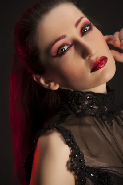 Portrait of beautiful young brunette woman in black dress against dark background, highlighted with red. Close-up portrait — Stock Photo, Image