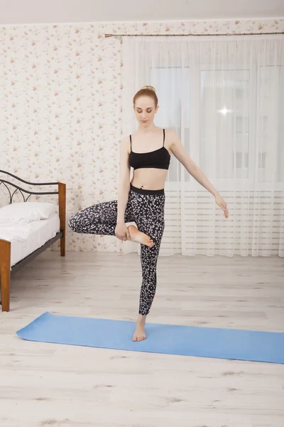 Hermosa joven practicando yoga estirándose en casa sobre una esterilla —  Fotos de Stock
