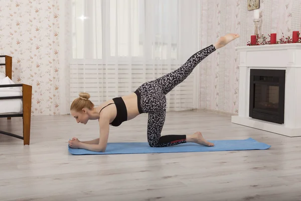 Hermosa joven practicando yoga estirándose en casa sobre una esterilla —  Fotos de Stock