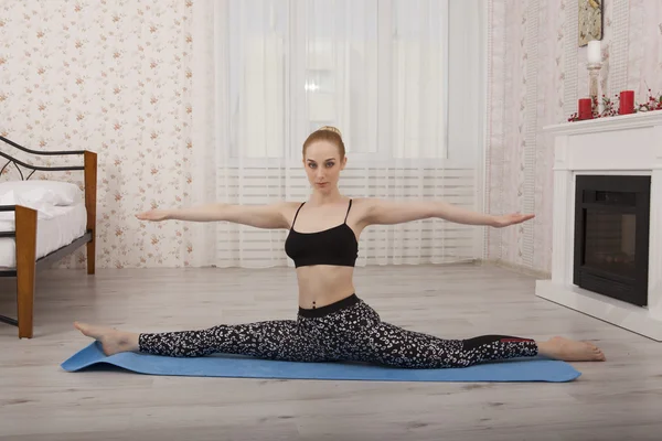 Hermosa joven practicando yoga estirándose en la esterilla haciendo splits —  Fotos de Stock