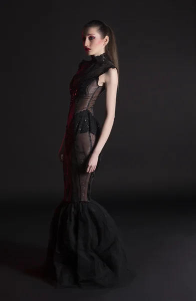 Portrait of beautiful young brunette woman in black dress against dark background, highlighted with red — Stock Photo, Image