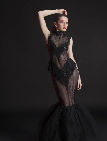 Portrait of beautiful young brunette woman in black dress against dark background, highlighted with red — Stock Photo, Image