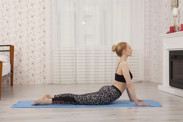 Hermosa joven practicando yoga estirándose en casa sobre alfombra - pose de cobra —  Fotos de Stock