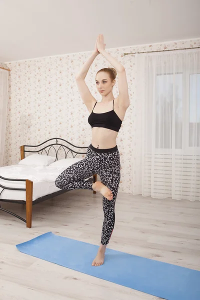 Hermosa joven practicando yoga estirándose en casa sobre una esterilla —  Fotos de Stock