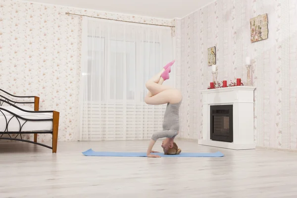Beautiful blonde woman practicing yoga stretching at home with blue mat in gray bodysuit, pink socks. Stand on arms and hands