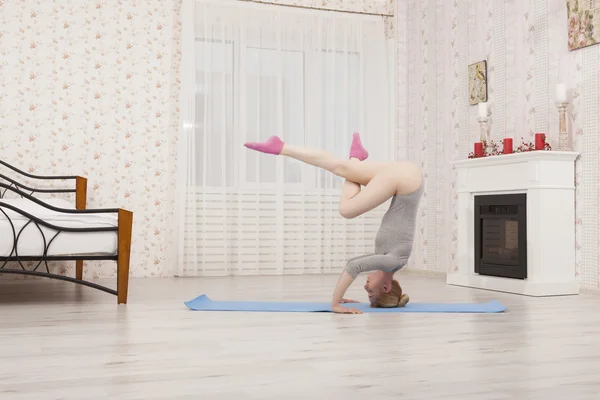 Hermosa mujer rubia practicando yoga estirándose en casa con esterilla azul en body gris, calcetines rosas. Párate en brazos y manos —  Fotos de Stock