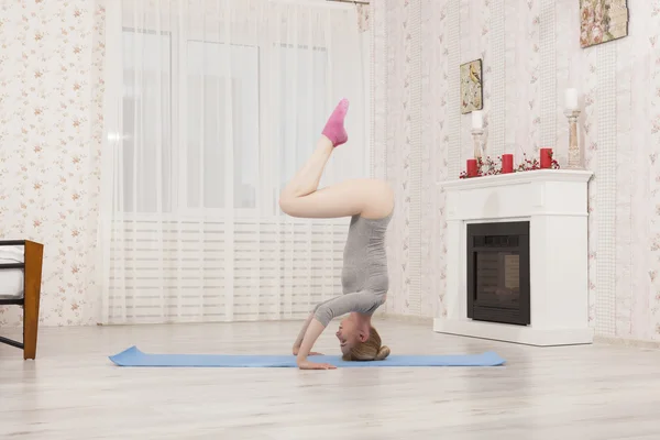 Hermosa mujer rubia practicando yoga estirándose en casa con esterilla azul en body gris, calcetines rosas. Párate en brazos y manos —  Fotos de Stock