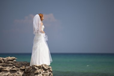 güzel gelin göz kamaştırıcı beyaz gelinlik içinde deniz cliff üzerinde duruyor.