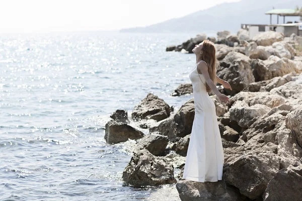 Linda noiva fica em um penhasco acima do mar em vestido de casamento branco glamourosa — Zdjęcie stockowe