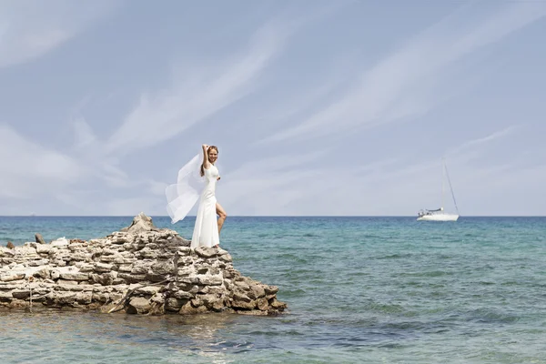 Linda noiva fica em um penhasco acima do mar em vestido de casamento branco glamourosa — Zdjęcie stockowe