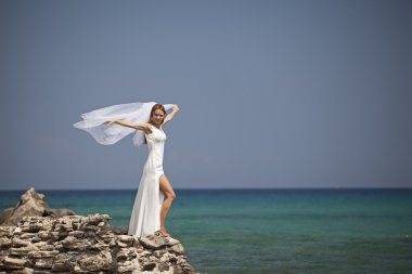 güzel gelin göz kamaştırıcı beyaz gelinlik içinde deniz cliff üzerinde duruyor.