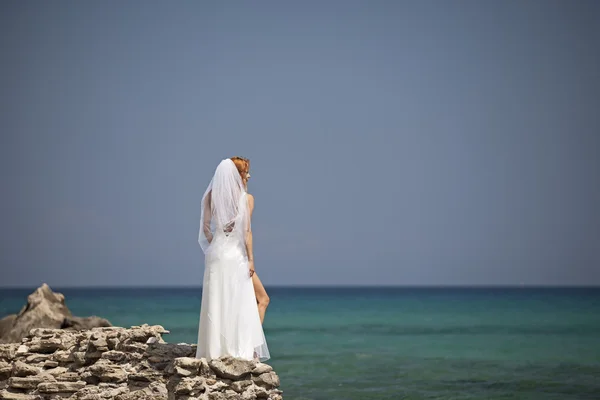 美しい花嫁は華やかな白いウェディング ドレスで海の上の崖上に立つ — ストック写真