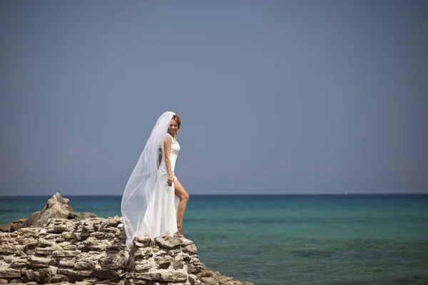 Linda noiva fica em um penhasco acima do mar em vestido de casamento branco glamourosa — Zdjęcie stockowe