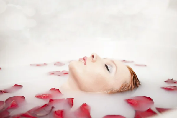 Portrait de beautyfull hot pinup girl, cheveux roux prenant un bain relaxant avec des pétales de fleurs sur fond d'espace de copie blanche — Photo